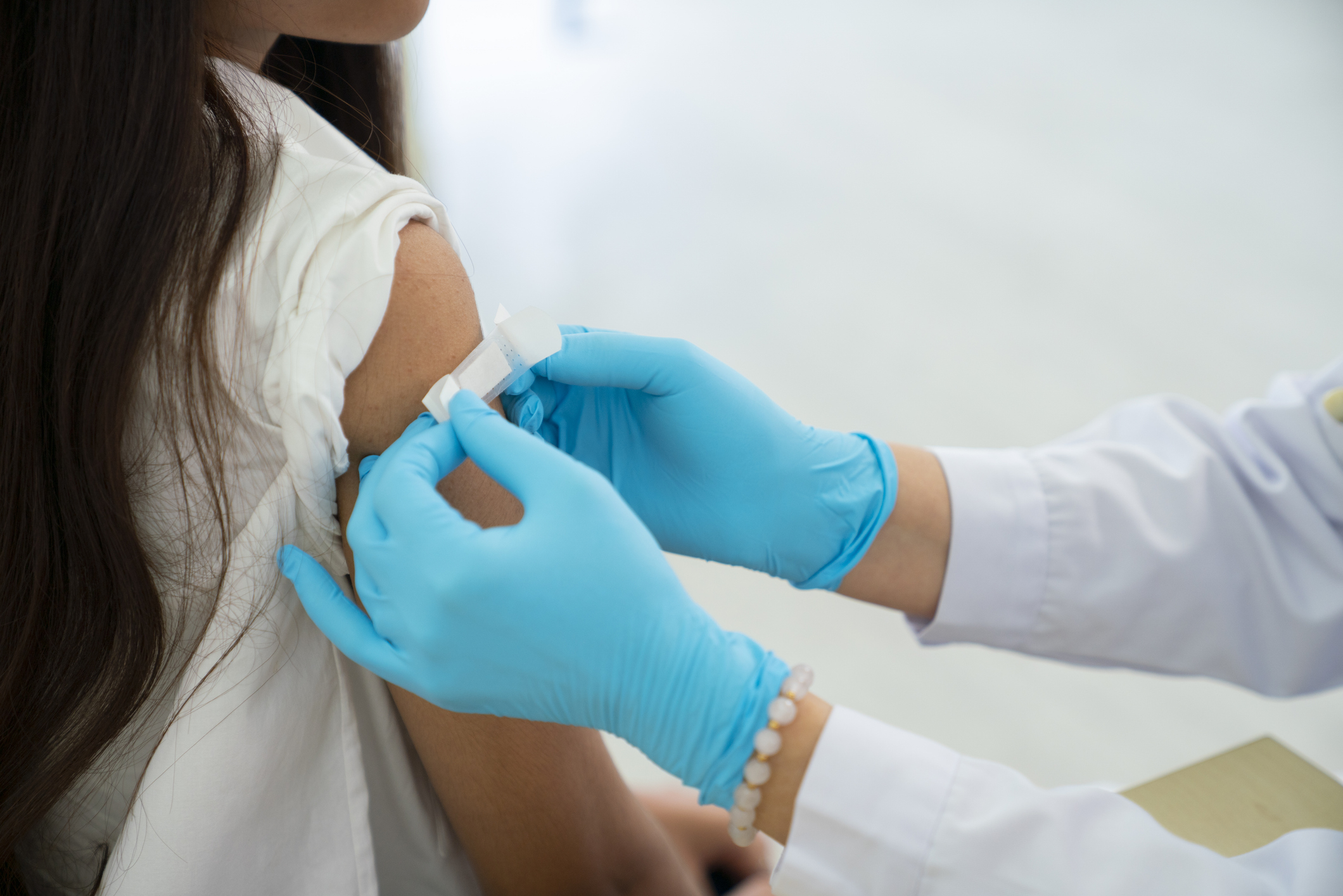 A healthcare professional wearing gloves applies a band-aid to a person&#x27;s arm after a vaccination
