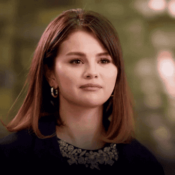 Selena Gomez nodding and then shaking her head gently, wearing a dark outfit with an embellished neckline, and medium-length hair