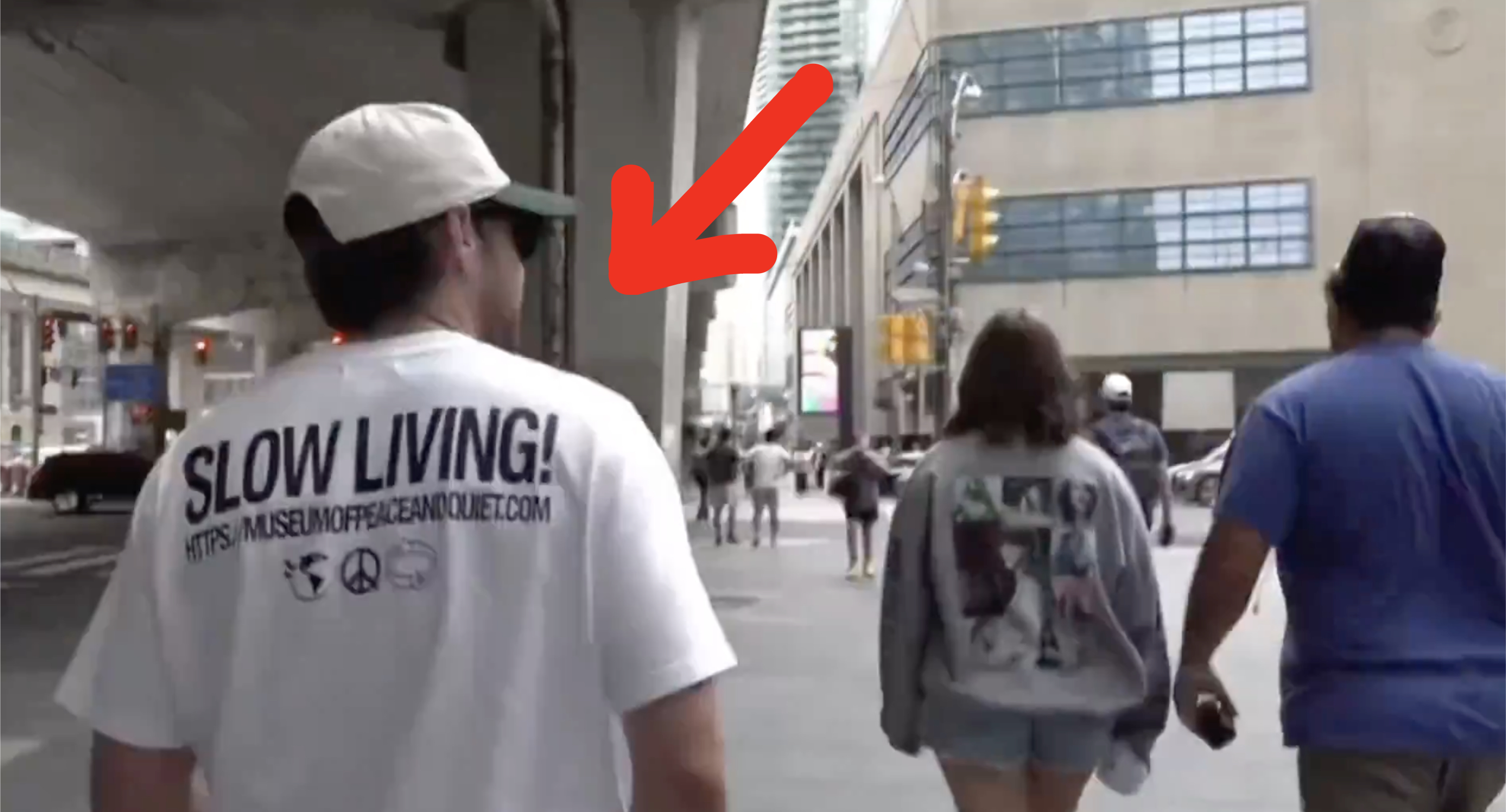 A man walks under an overpass in a shirt that says &quot;SLOW LIVING!&quot; followed by peace sign and recycling symbols