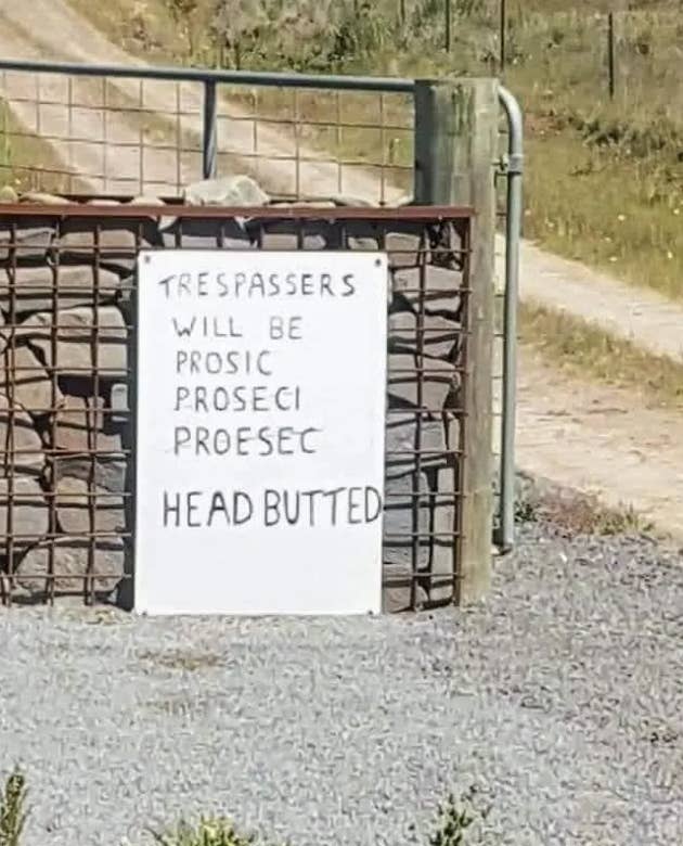 A handwritten sign on a gate reads, &quot;Trespassers will be prosic proseci proesec head butted.&quot; It appears to warn trespassers with humor