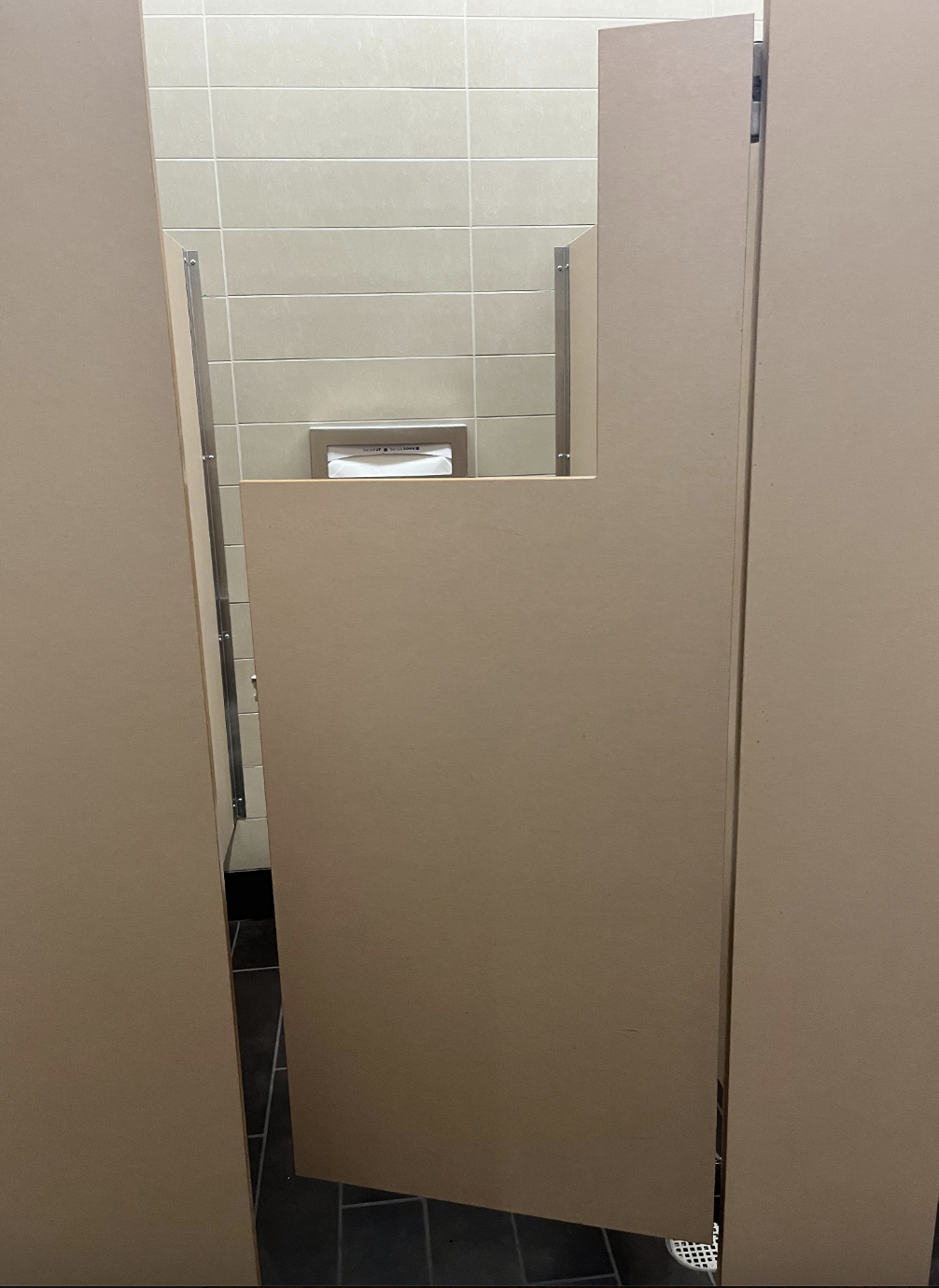 Bathroom stall with a door cut to fit around a high toilet paper dispenser, revealing the lack of privacy