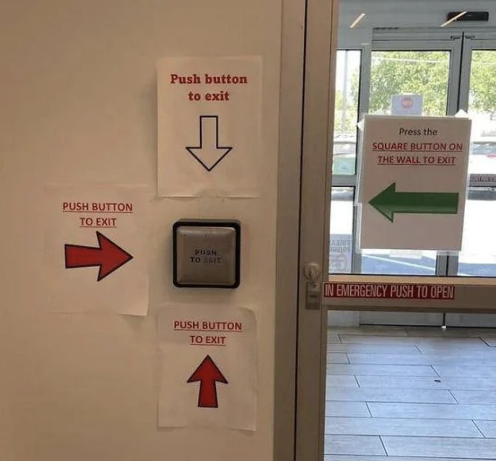 Exit instructions on a door with multiple signs: push buttons to exit, marked by red arrows, and press a square button on the wall to exit, marked by a green arrow