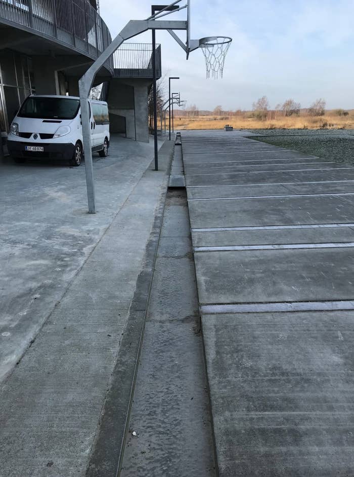 Unusual basketball court with hoops installed horizontally along a parking lot. A white van is parked nearby