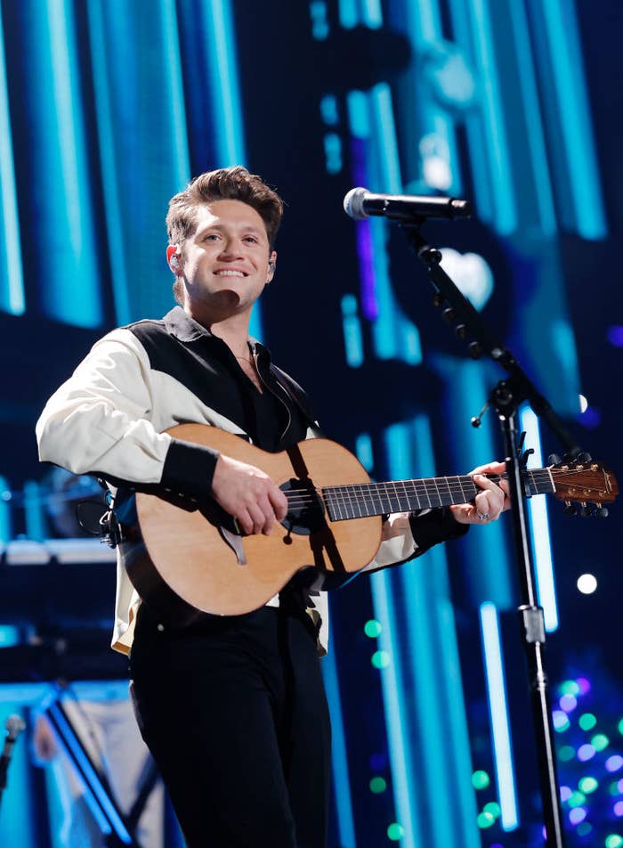 Niall Horan performs on stage with a guitar, wearing a stylish black and white jacket, during a music event