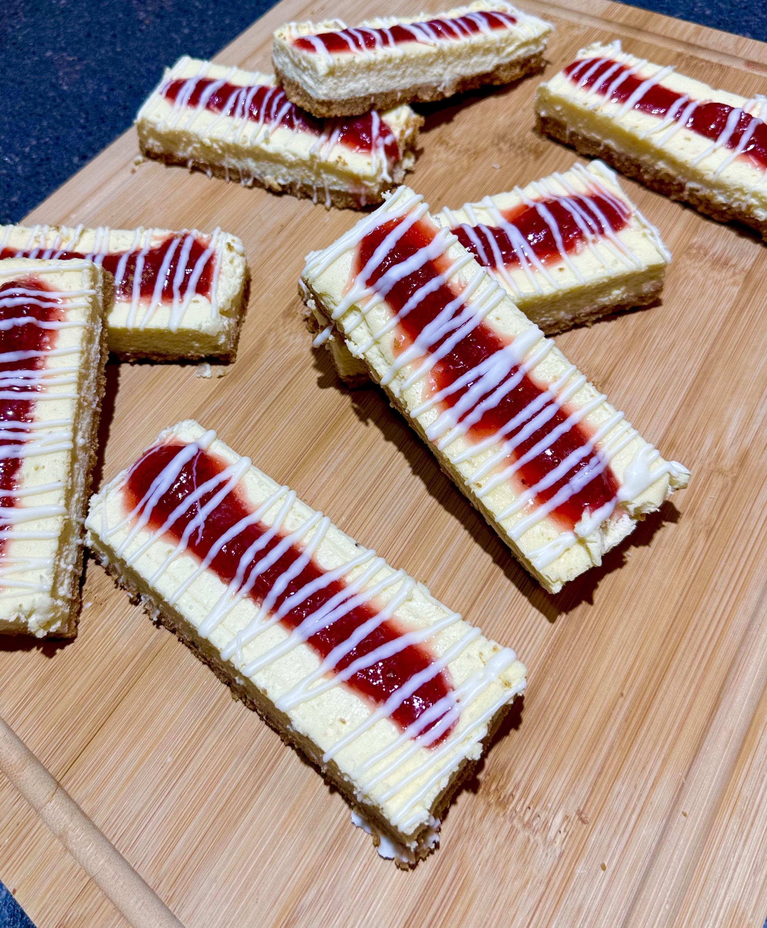 Rectangular dessert bars on a wooden board topped with white and red icing drizzles