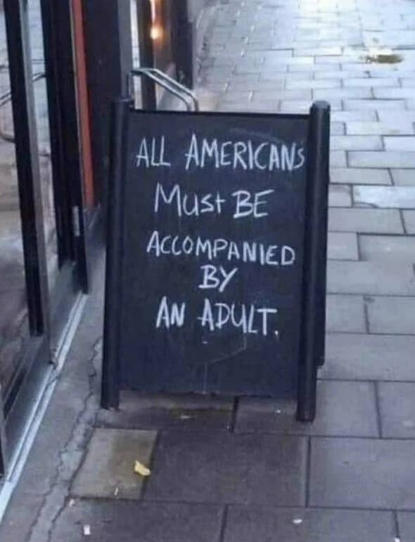 Sign on a sidewalk reads, &quot;ALL AMERICANS MUST BE ACCOMPANIED BY AN ADULT.&quot;