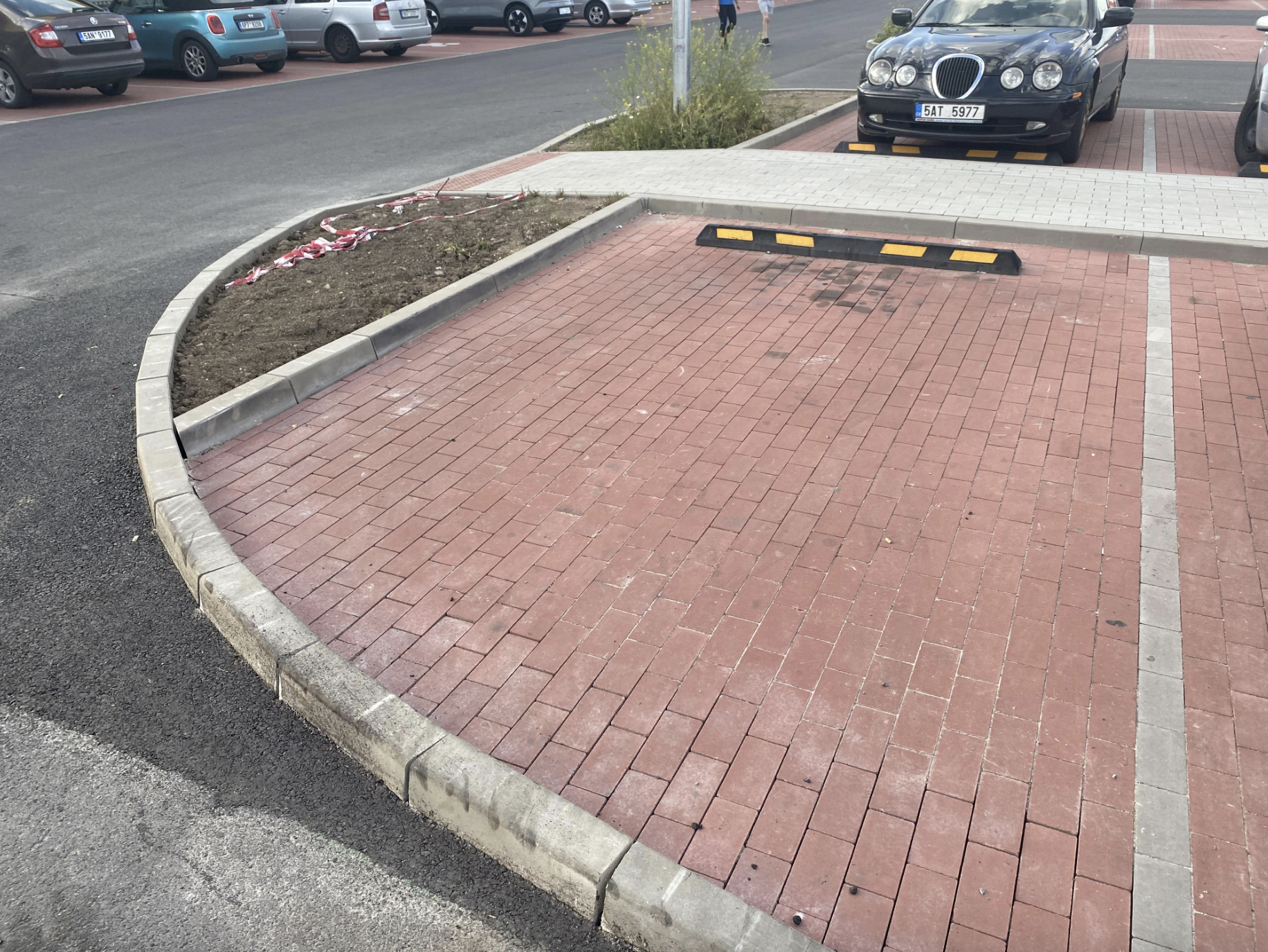 A photo of an empty, curved brick parking space near a street, with a black car parked in the adjacent space