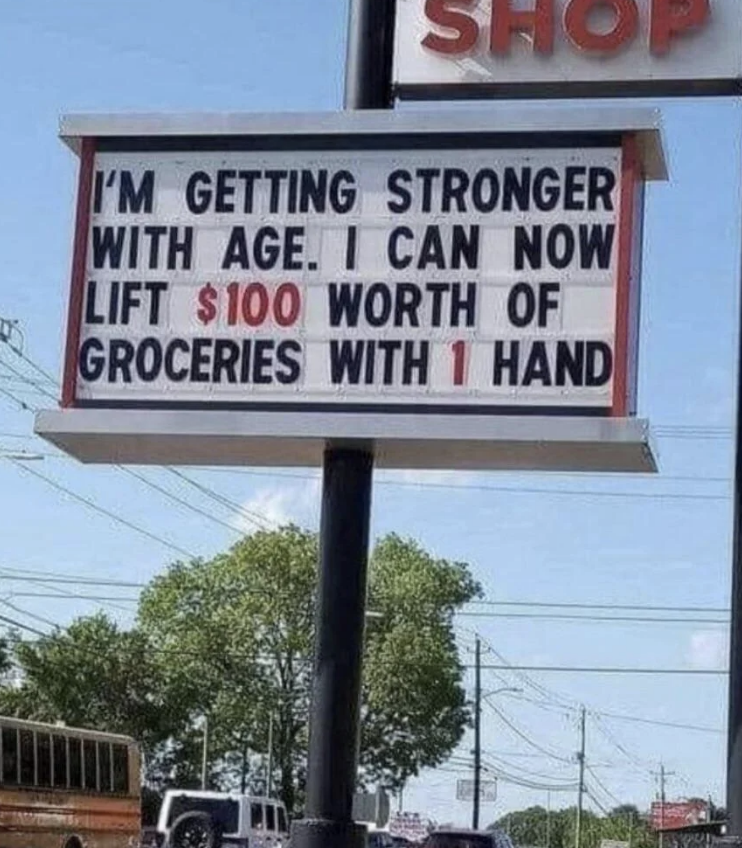 Sign reads: &quot;I&#x27;M GETTING STRONGER WITH AGE. I CAN NOW LIFT $100 WORTH OF GROCERIES WITH 1 HAND.&quot;