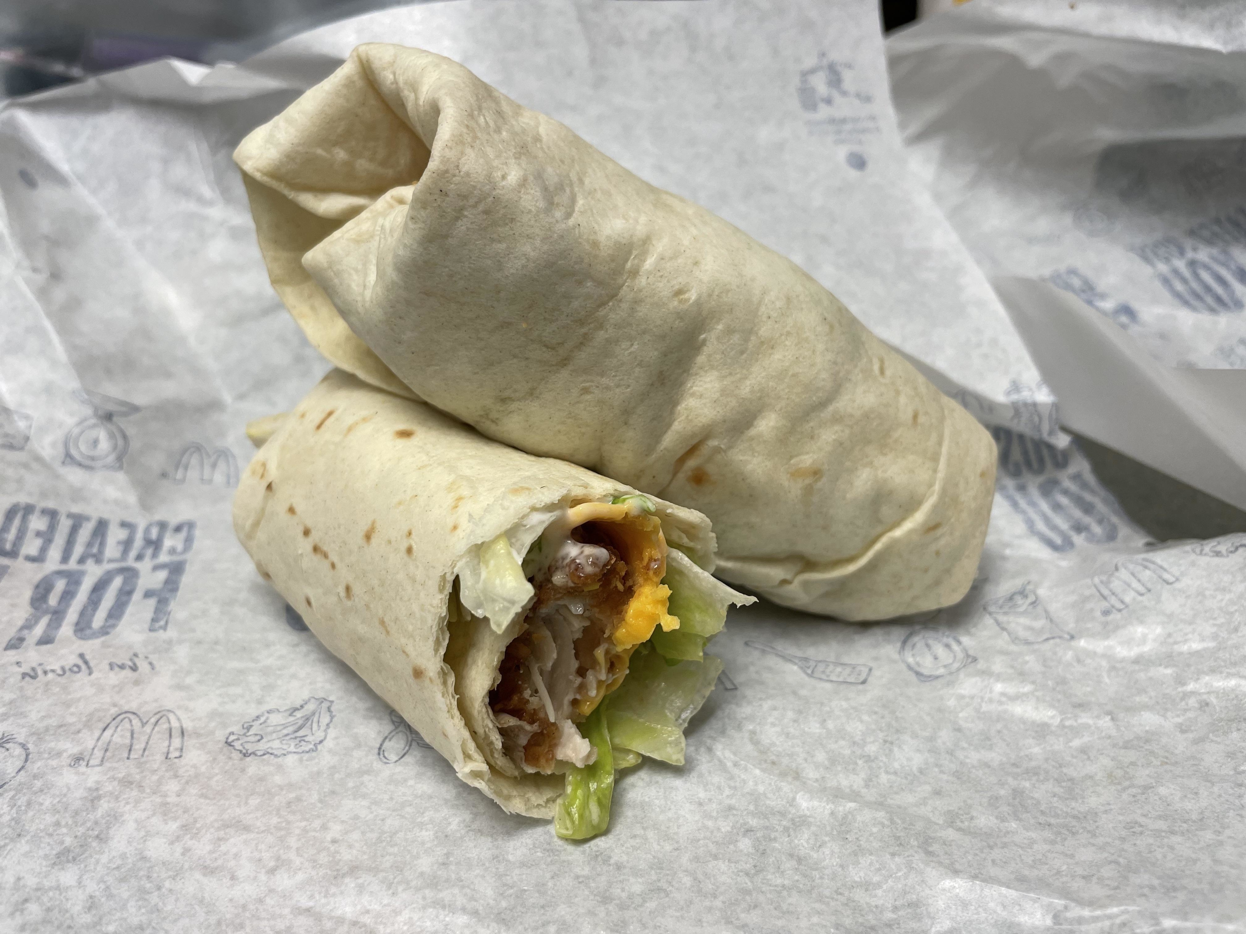 A cut burrito with visible ingredients such as lettuce, bacon, and cheese sits on McDonald&#x27;s branded paper