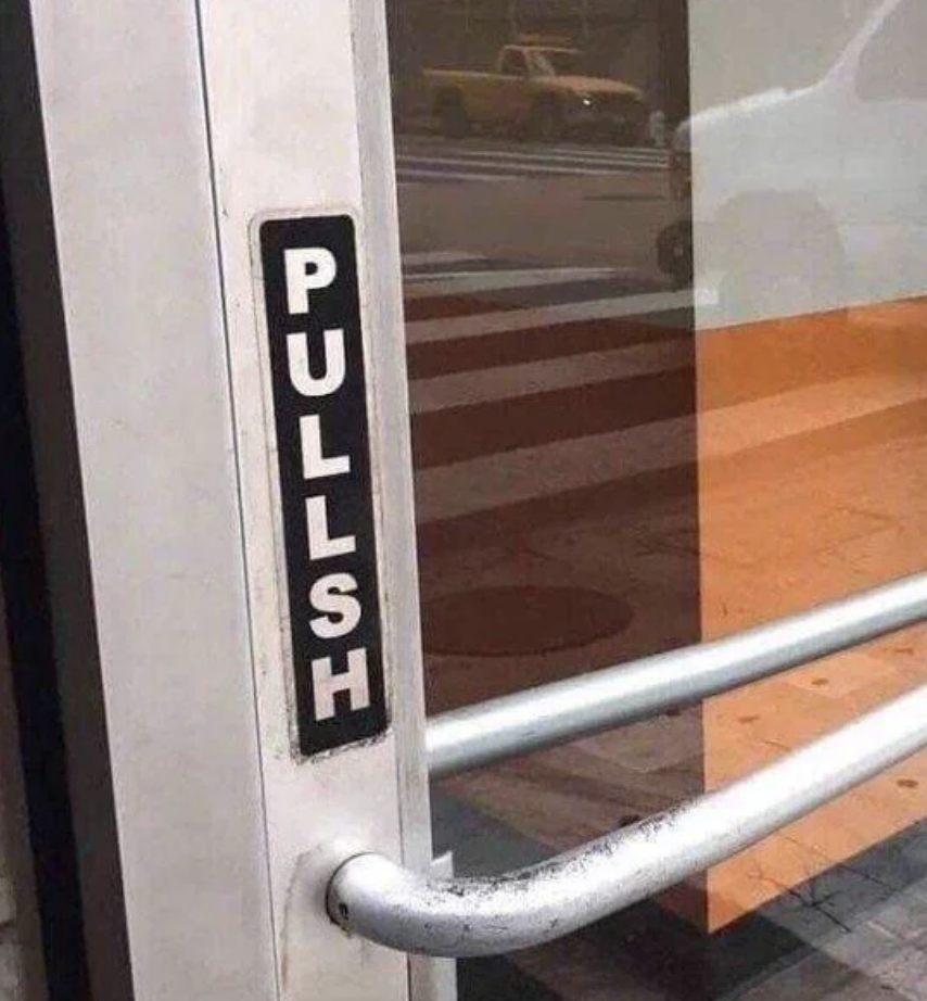 Sign on a glass door reads &quot;PULLSH&quot; instead of &quot;PULL.&quot; A person is visible outside by the crosswalk. A humorous misspelling of the word &quot;PULL.&quot;