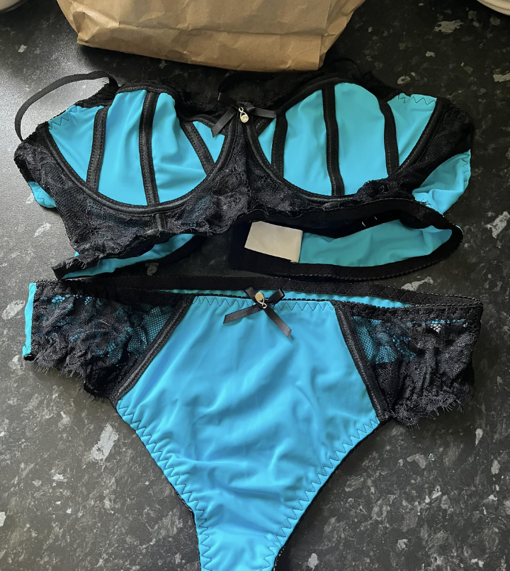 A set of blue and black lace lingerie, consisting of a bra and panties, placed on a dark surface