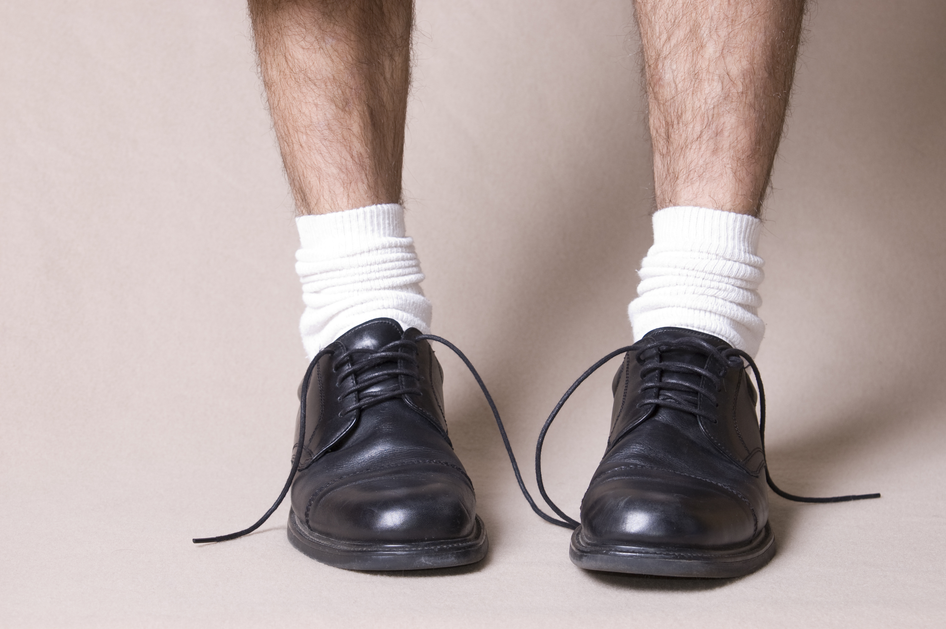 Close-up of a person&#x27;s legs wearing white socks and black dress shoes with untied laces. The focus is on the shoes and socks, illustrating a casual or unfinished look