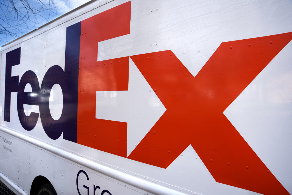 FedEx delivery truck seen in profile, displaying the company&#x27;s logo prominently on the side against an urban backdrop