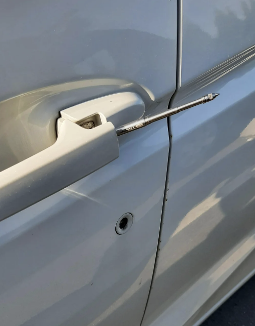 A car door handle with a screwdriver inserted behind it, possibly indicating an attempted break-in or repair