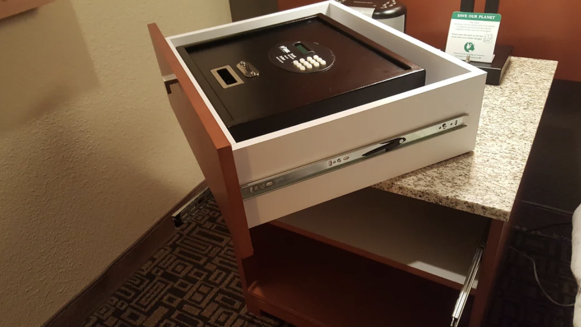 A hotel safe is pulled out of a drawer, revealing the inside of the drawer beneath it. The safe has a digital keypad on top
