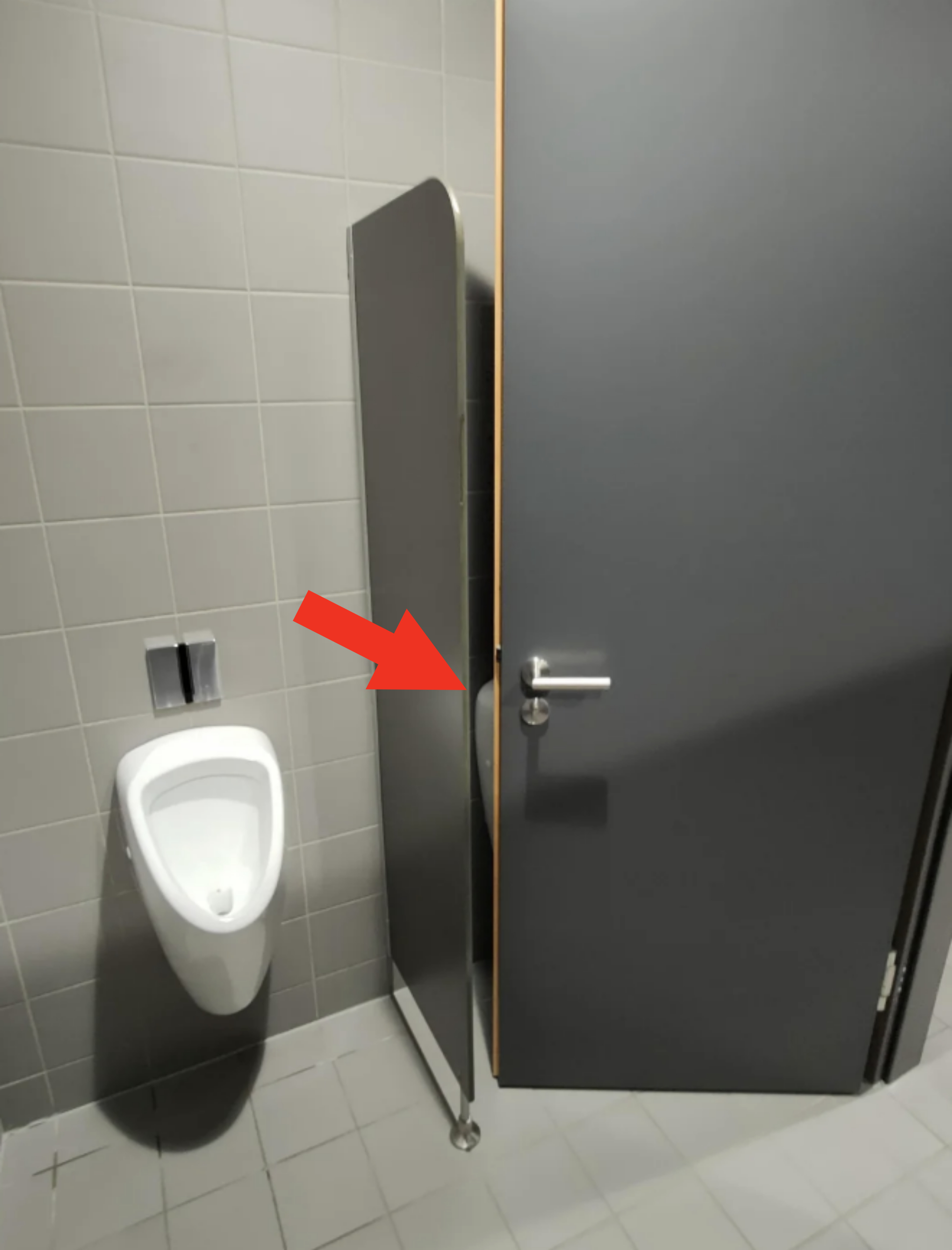 A urinal partially obstructed by a stall door in a restroom