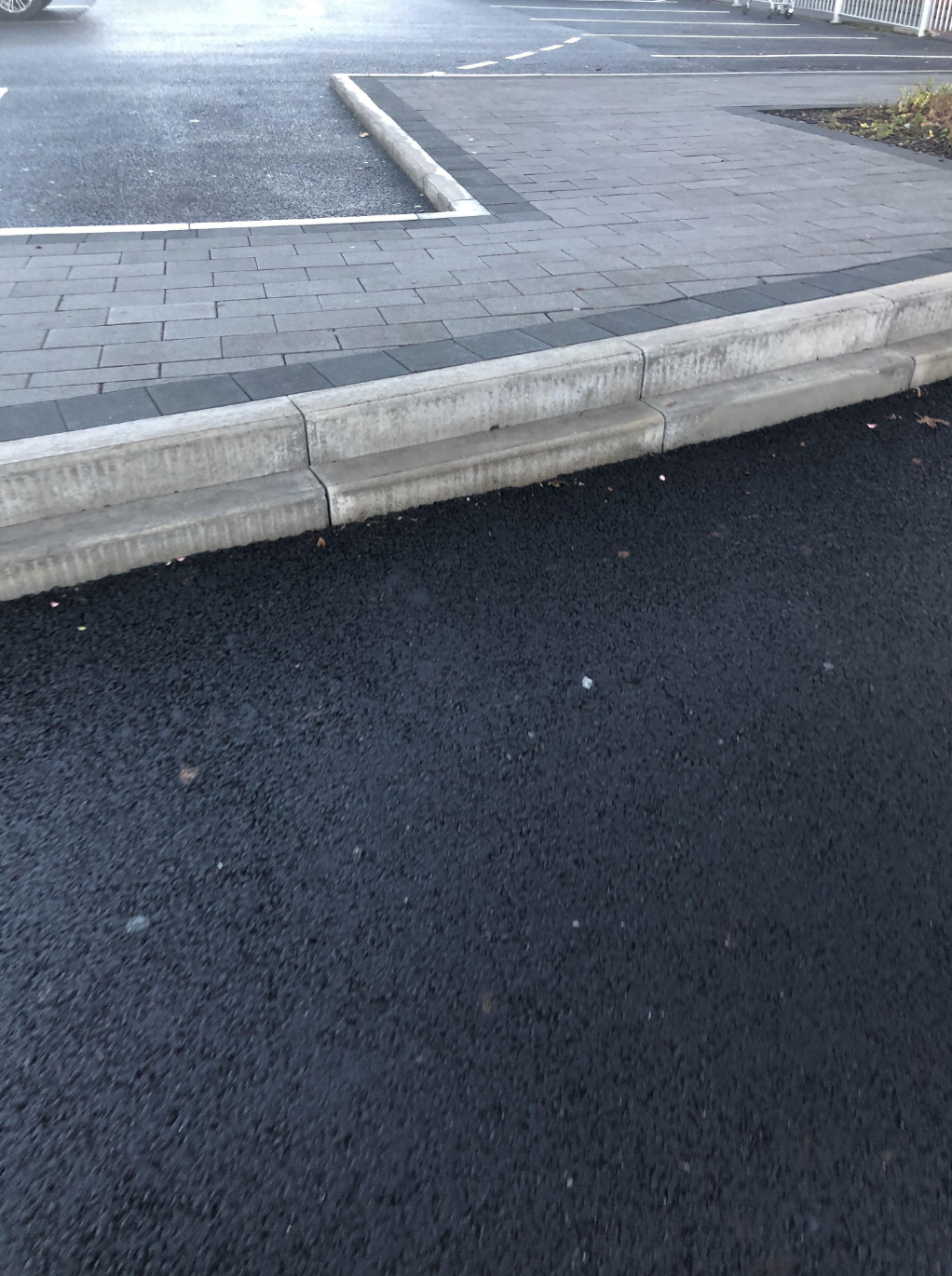 A parking lot curb with uneven pavement, possibly hazardous for pedestrians or vehicles