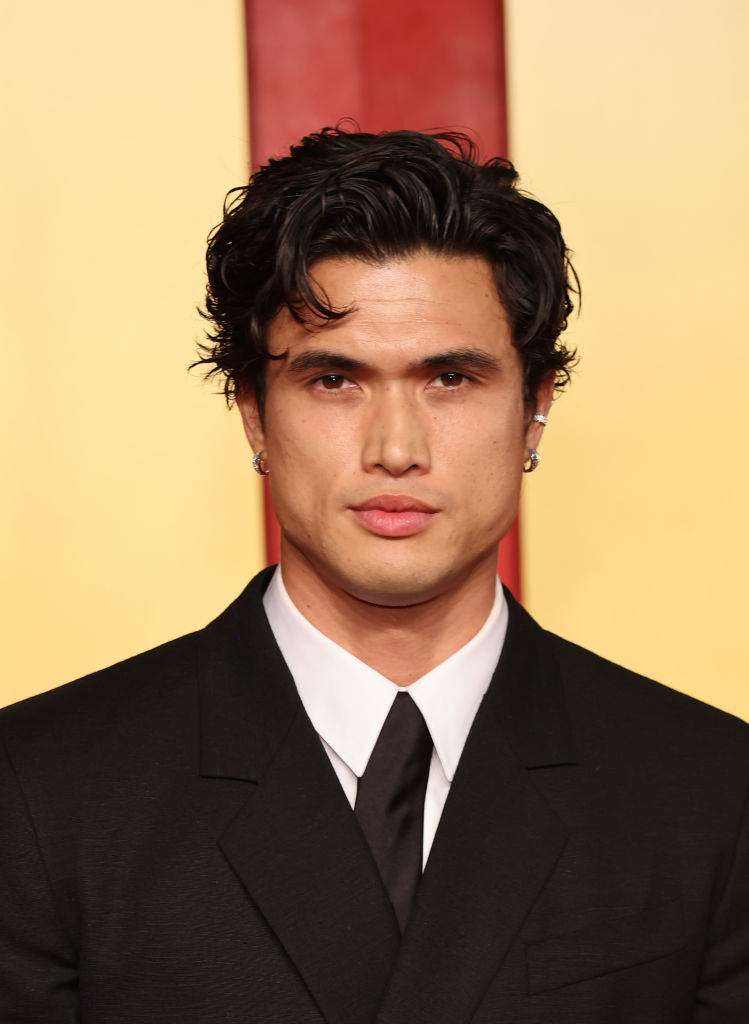 A man with short dark hair, wearing a black suit and tie, poses for a photo