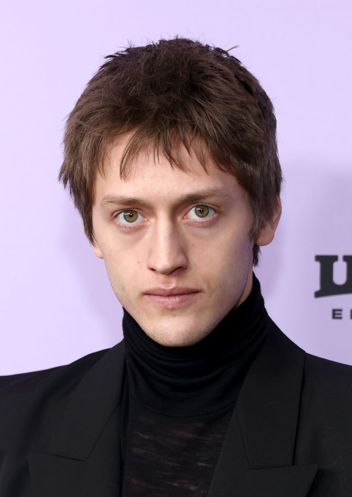 Young man in black turtleneck and black blazer at an event. His serious expression is directed at the camera