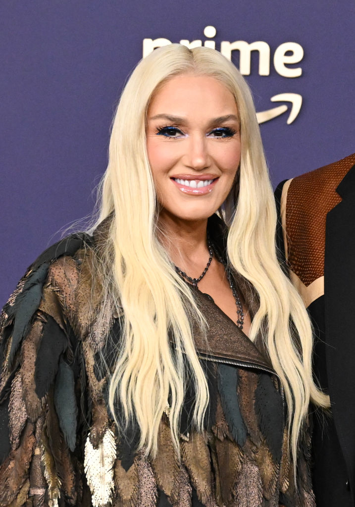 Gwen Stefani on a red carpet, wearing a fringed, textured jacket. She smiles at the camera. The &quot;Prime&quot; logo is visible in the background