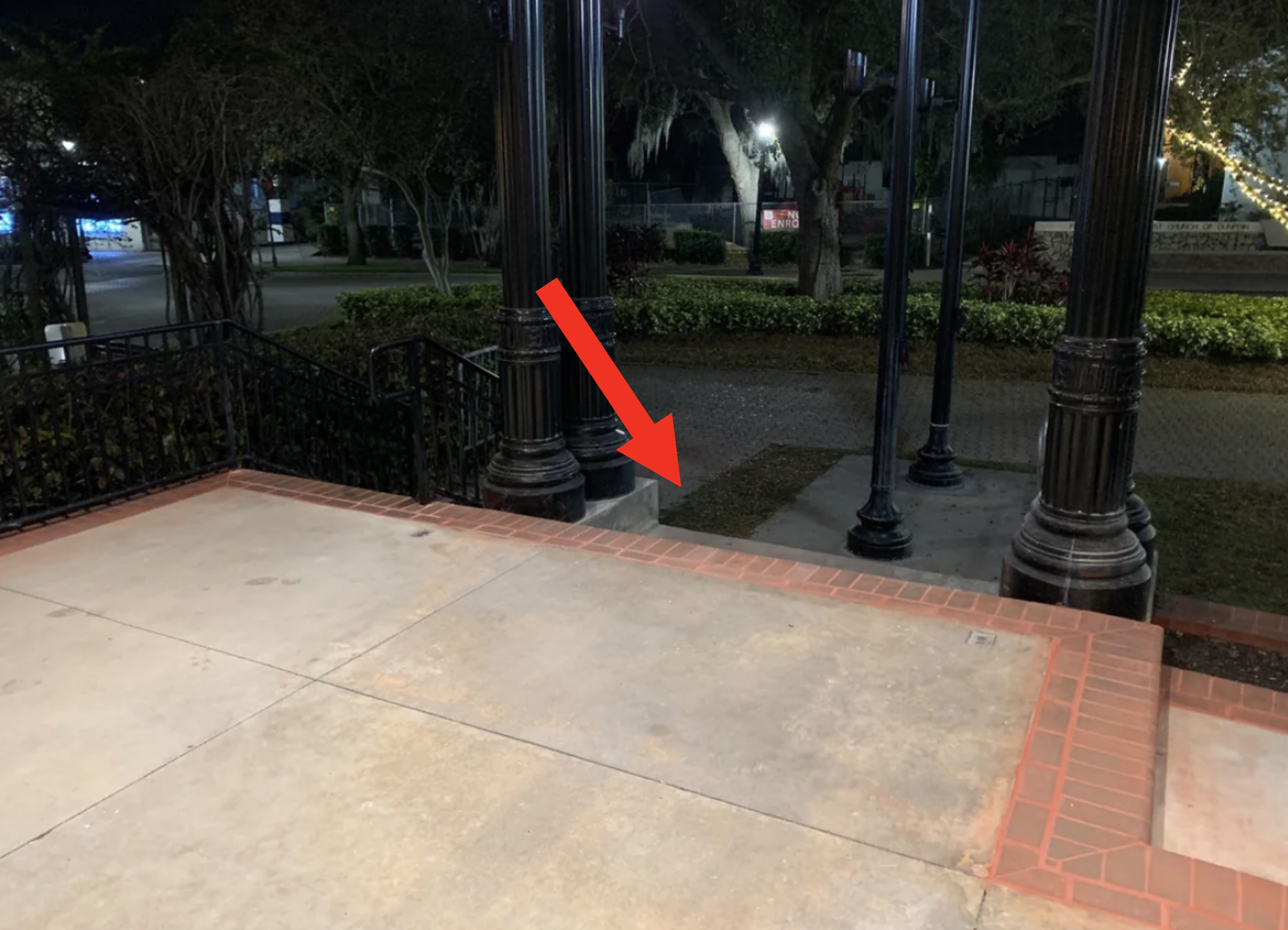 Empty concrete stage with four tall columns, metal railings, and surrounding trees in a park at night