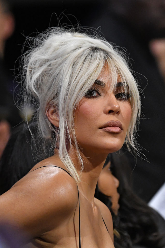 Kim Kardashian with platinum blonde hair in an elegant updo, wearing a strapless dress at a public event, looking over her shoulder