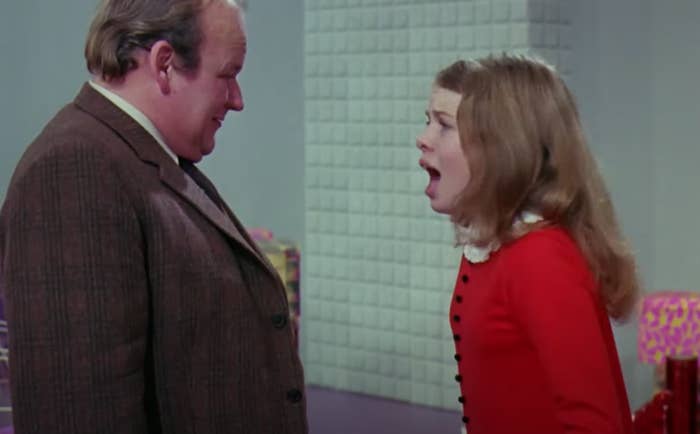 Veruca Salt, wearing a red dress, is yelling at a man in a tweed suit in a scene from &quot;Willy Wonka &amp;amp; the Chocolate Factory.&quot;
