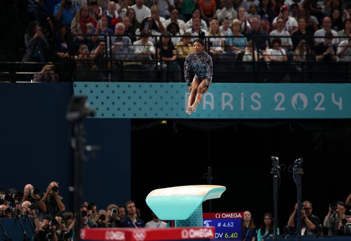 Simone Biles performs a vault at the Paris 2024 gymnastics competition, observed by an audience of spectators and photographers