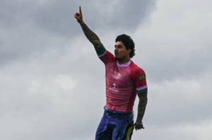 Gabriel Medina is surfing, raising his left arm, with one finger pointing up, celebrating a victory