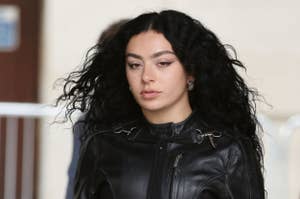 Charli XCX with wavy hair, wearing a leather jacket, is seen walking