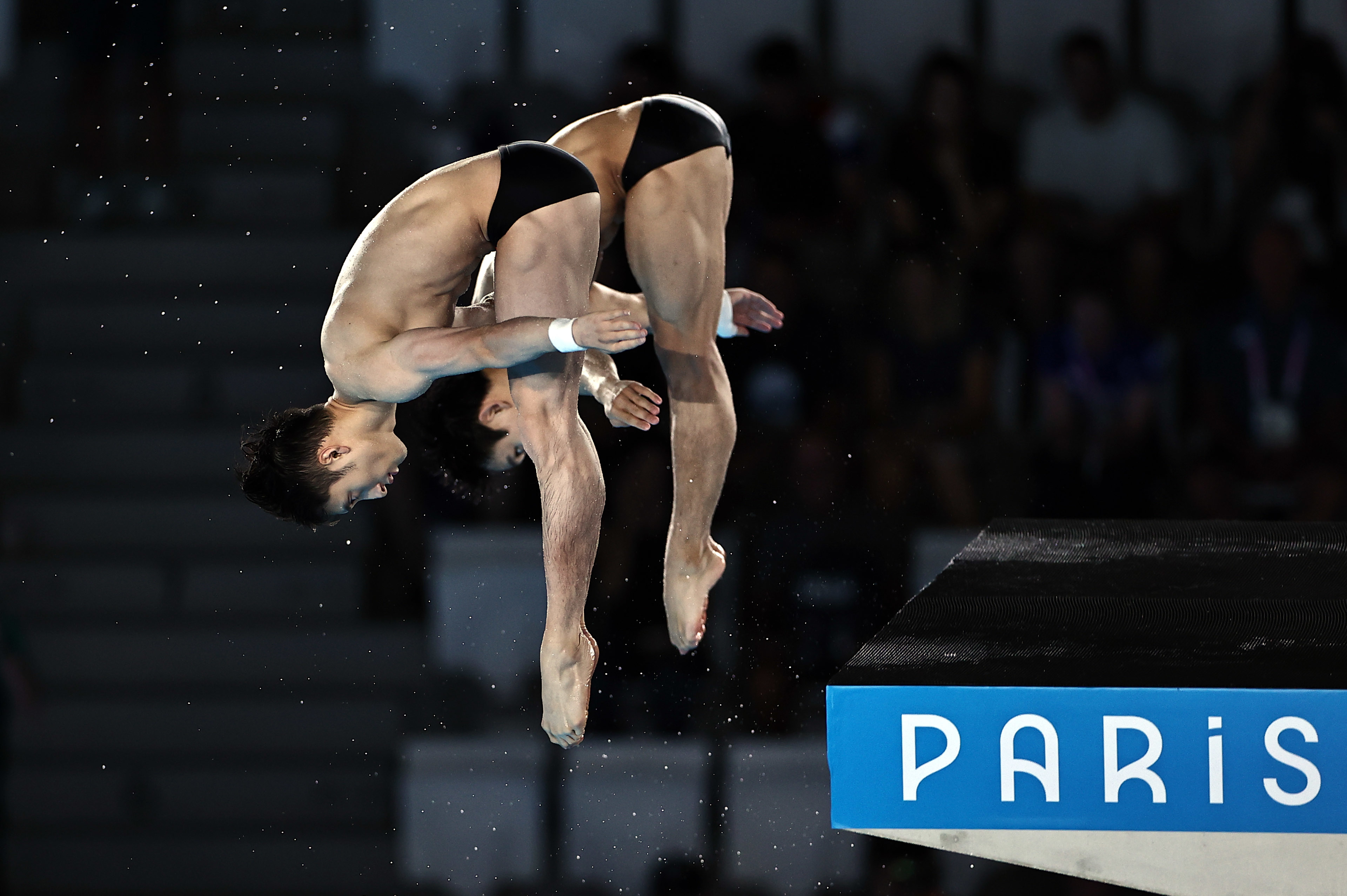 Two male divers, mid-dive in synchronized form, are competing at an event in Paris