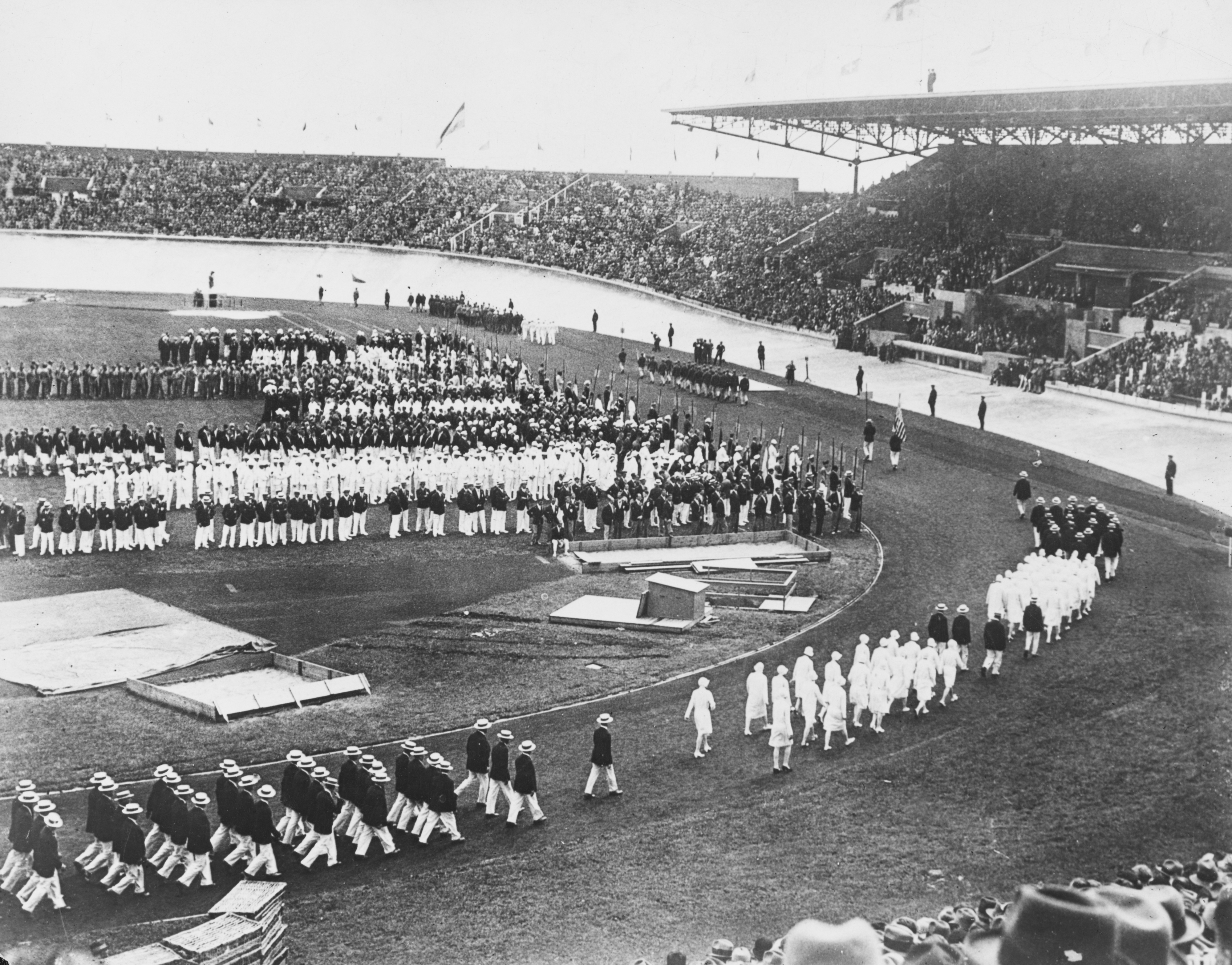 Overview of a stadium filled with spectators, watching athletes parade in formation at an Olympic event