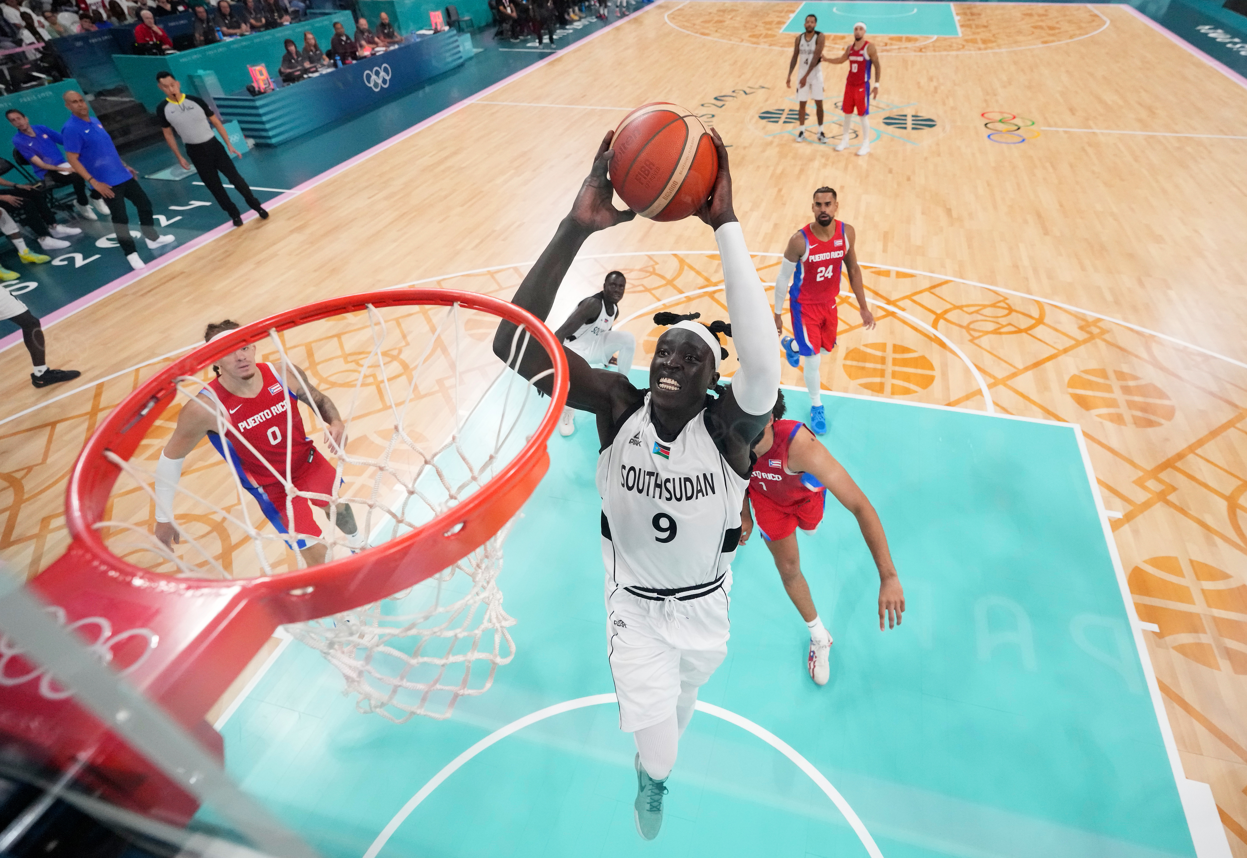 Basketball game with South Sudan&#x27;s player dunking, wearing jersey number 9. Opponents from Puerto Rico, in red jerseys, and South Sudan players are visible