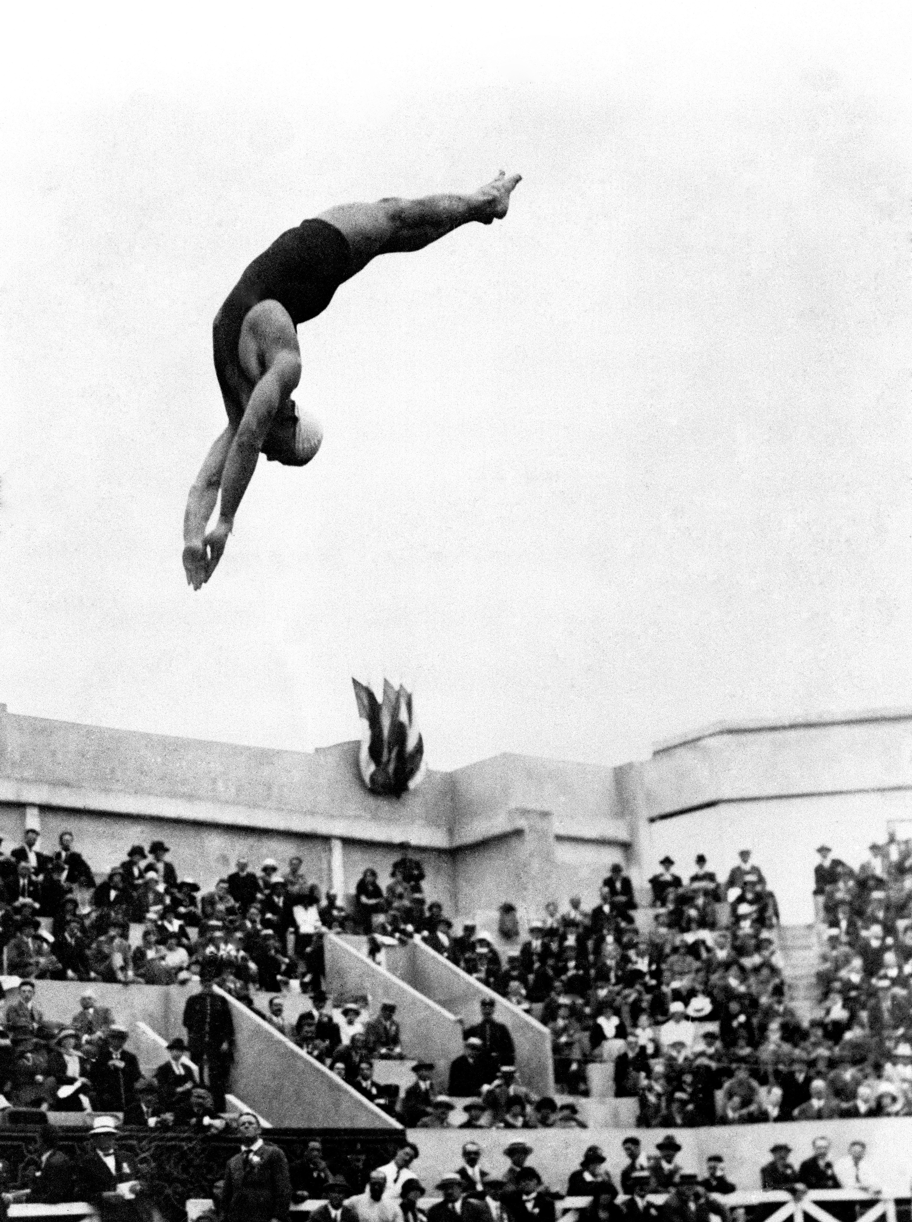 A diver is captured mid-air, performing a dive in front of an audience at an outdoor event