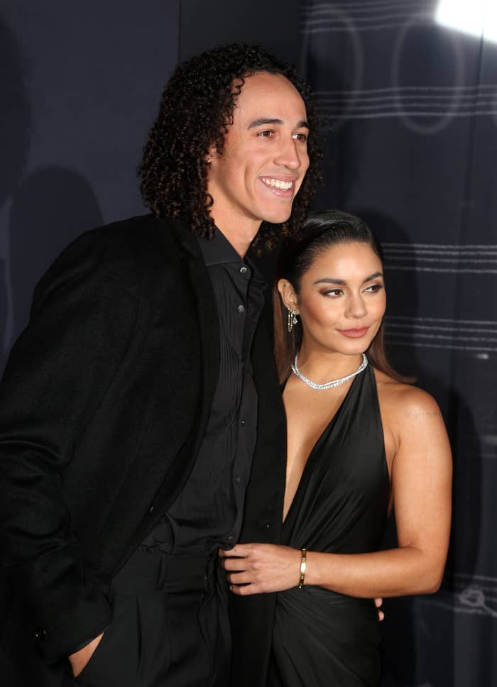 Vanessa Hudgens in an elegant halter dress, standing with Cole Tucker, who is wearing a suit on the red carpet