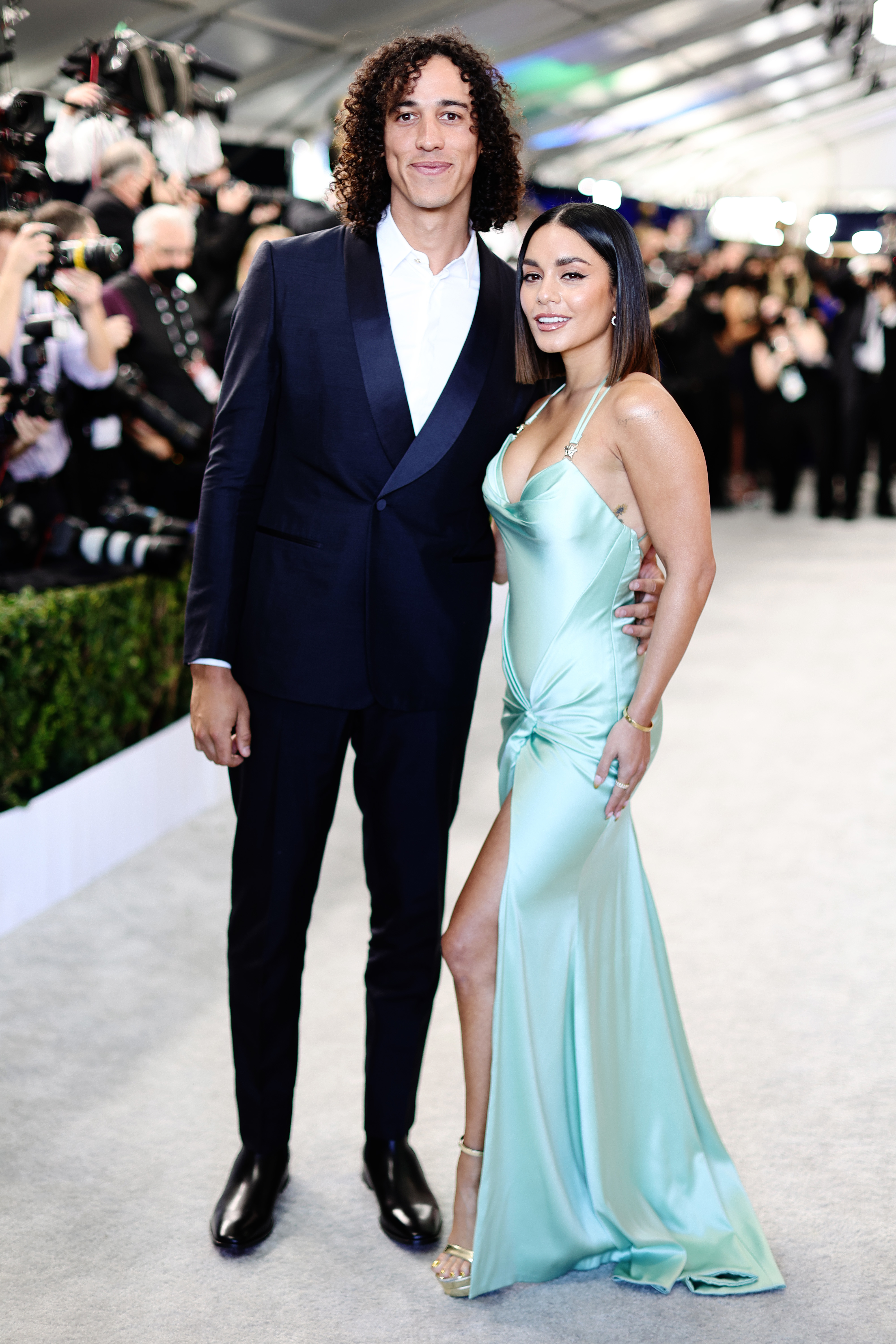 Cole in a tuxedo and Vanessa Hudgens in a stylish, form-fitting satin gown with a thigh-high slit pose on a red carpet