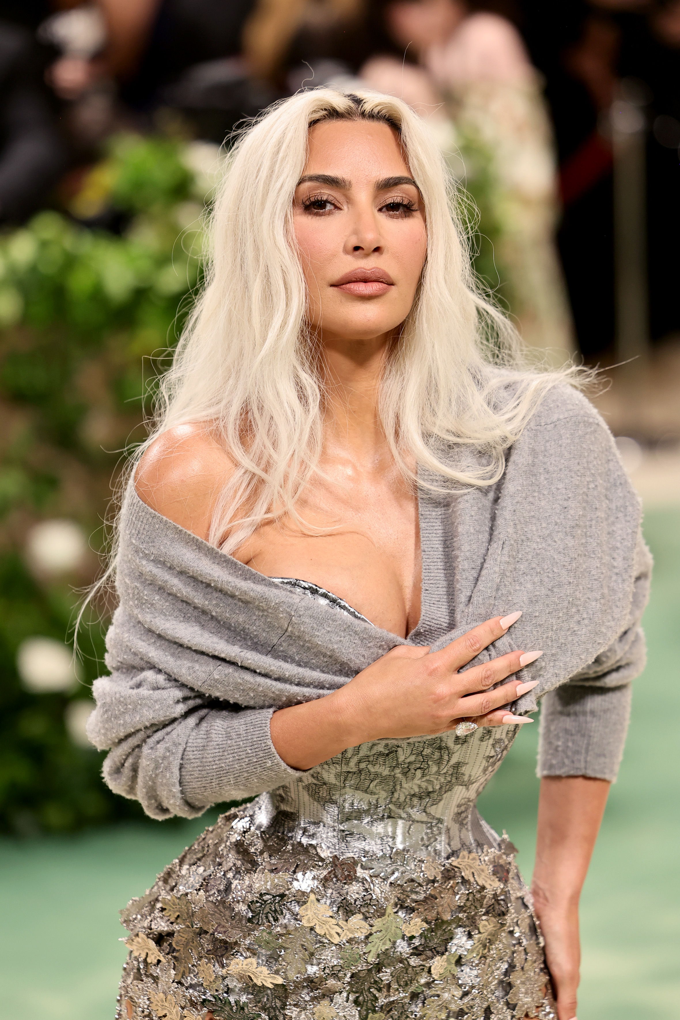 Kim Kardashian in an off-the-shoulder sweater with a metallic, floral-patterned skirt, poses on the red carpet