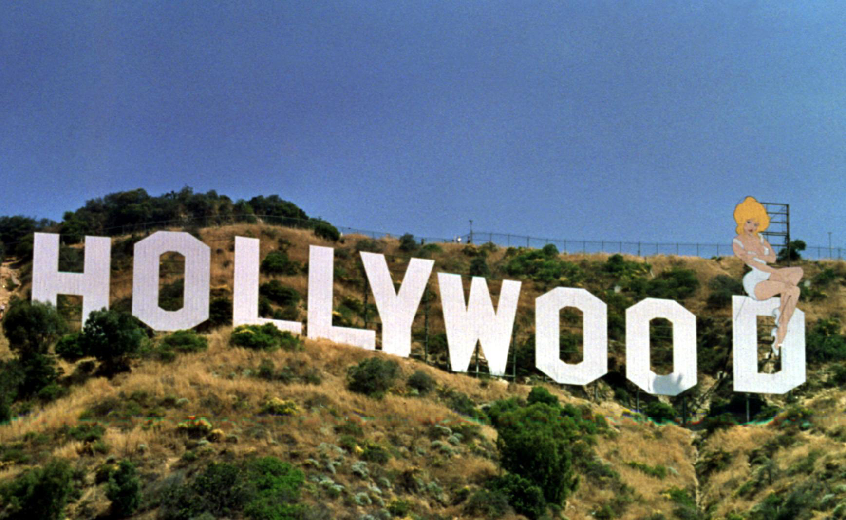 The Hollywood sign on a hillside, modified with a cartoon of Marilyn Monroe sitting on the last letter &#x27;D&#x27;