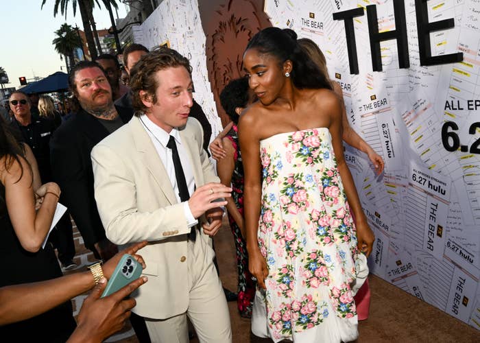 Jeremy Allen White and Ayo Edebiri interact at the premiere event for &quot;The Bear,&quot; with Ayo wearing a floral dress and Jeremy in a beige suit