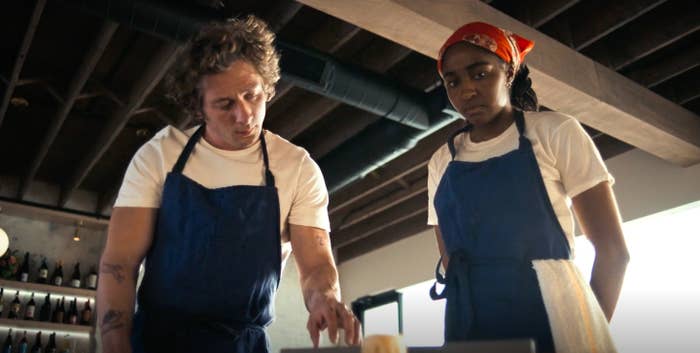 Jeremy Allen White and Ayo Edebiri, wearing aprons, appear focused while working in a kitchen