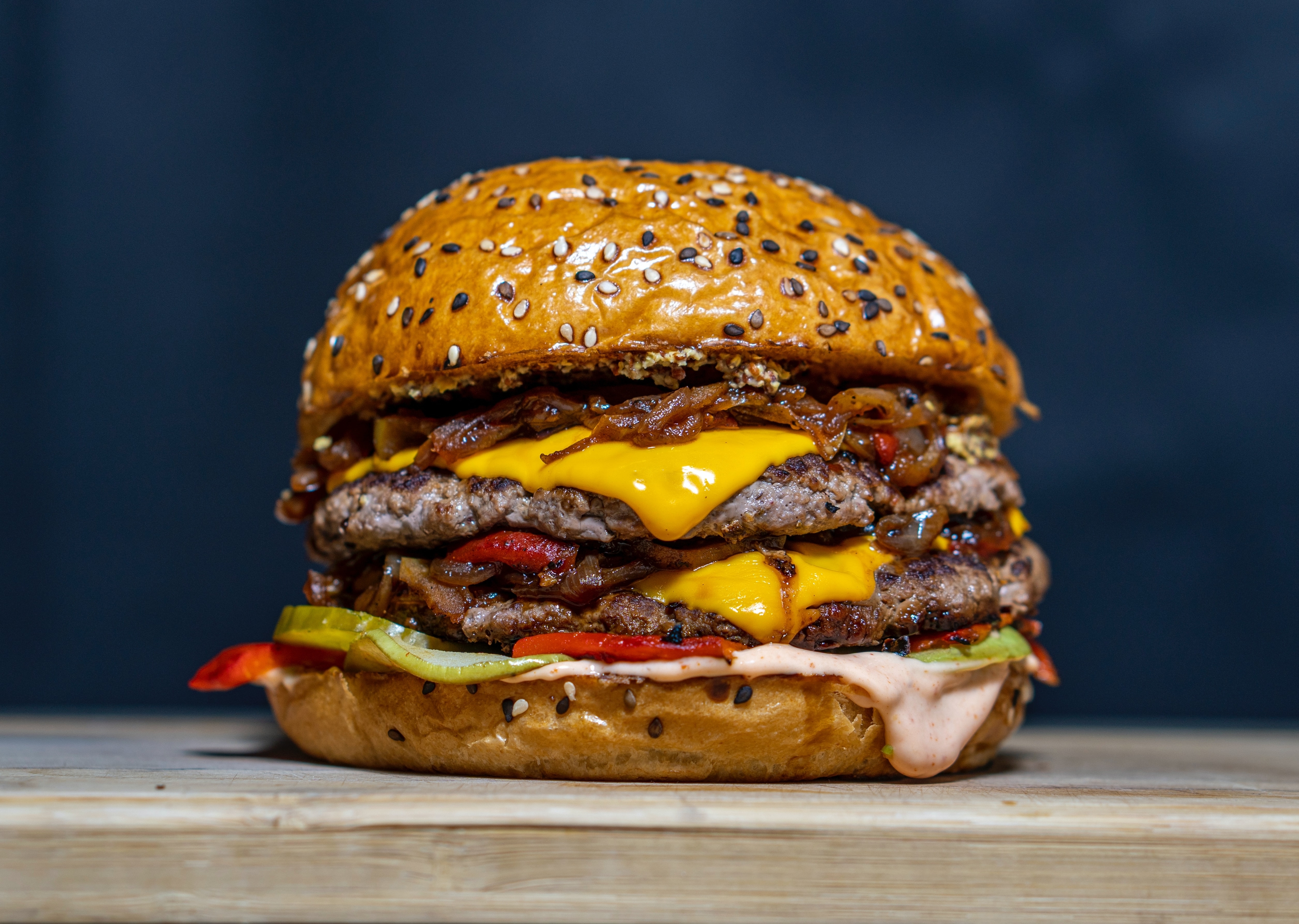 Close-up of a juicy double cheeseburger with bacon, pickles, and sauce on a sesame seed bun