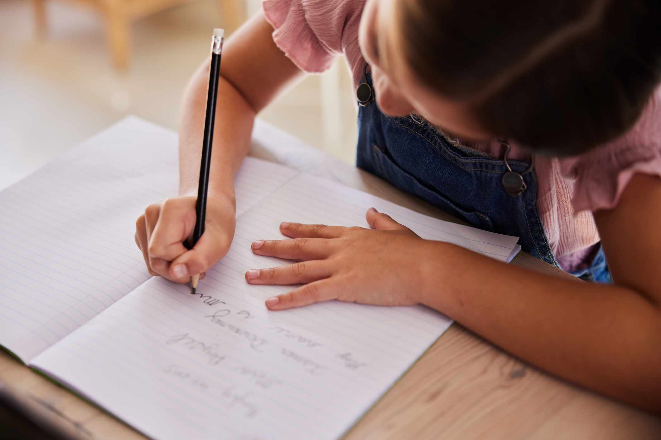 A young child writing in a notebook, focusing intently on their work, dressed casually with short sleeves