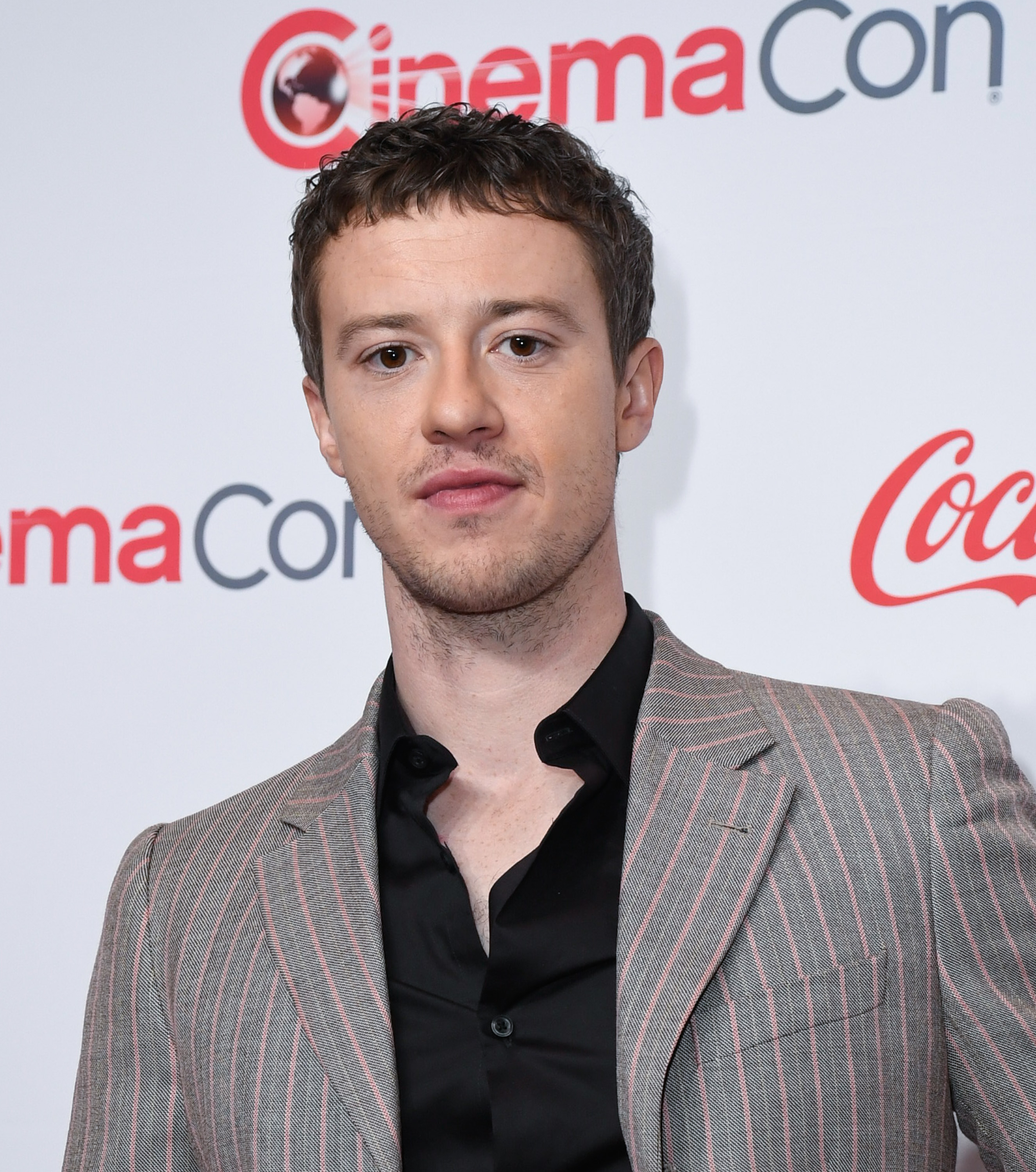 Joseph Quinn poses for a photo at CinemaCon, wearing a pinstriped suit over a black shirt