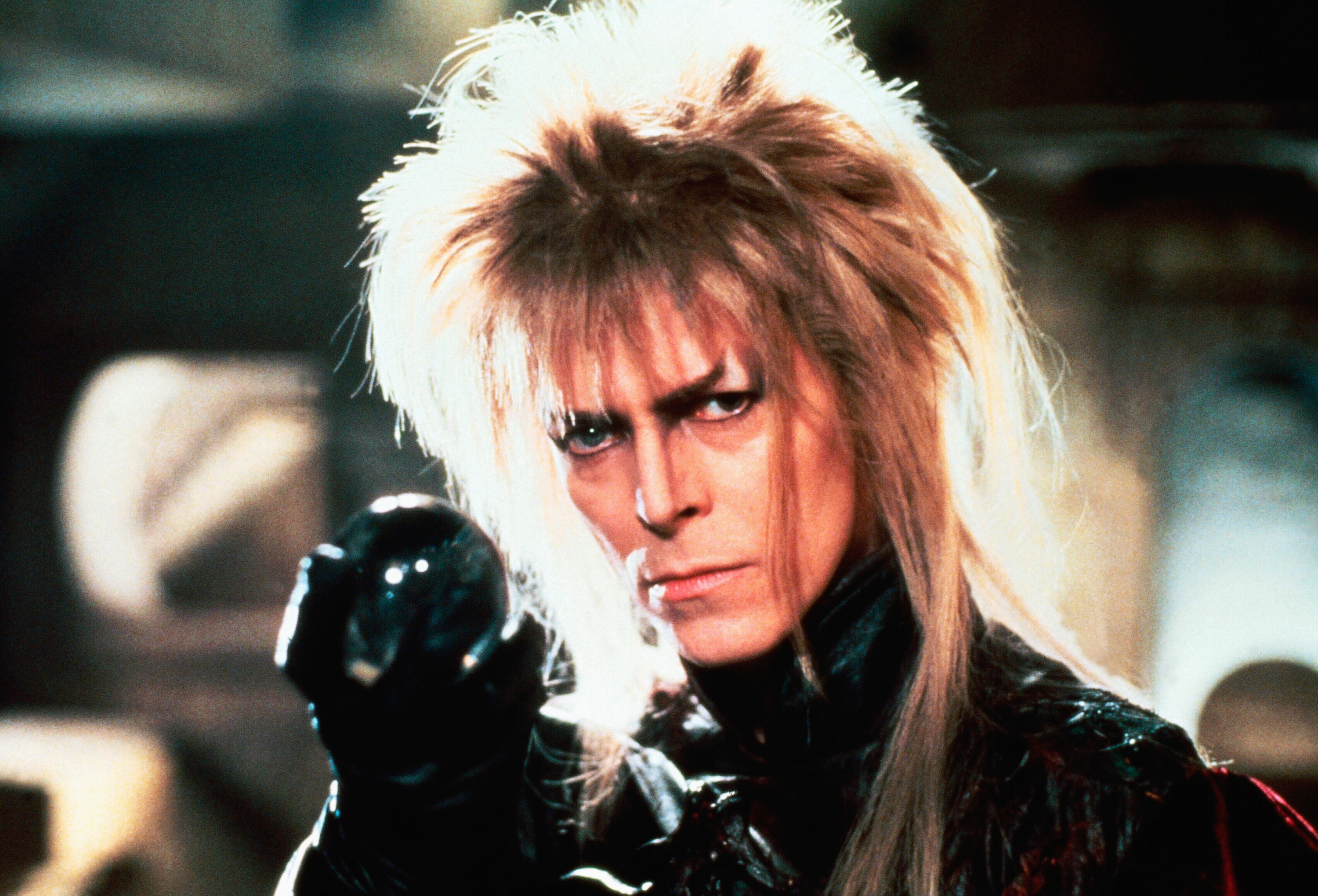 David Bowie in &quot;Labyrinth&quot; with spiked hair and dramatic makeup, wearing dark, fantasy-styled clothing and gloves, holding a crystal ball