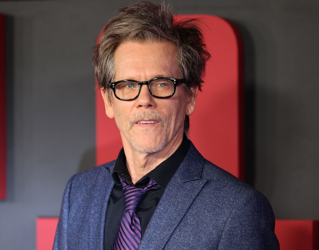 Kevin Bacon wearing a suit and tie, standing on the red carpet