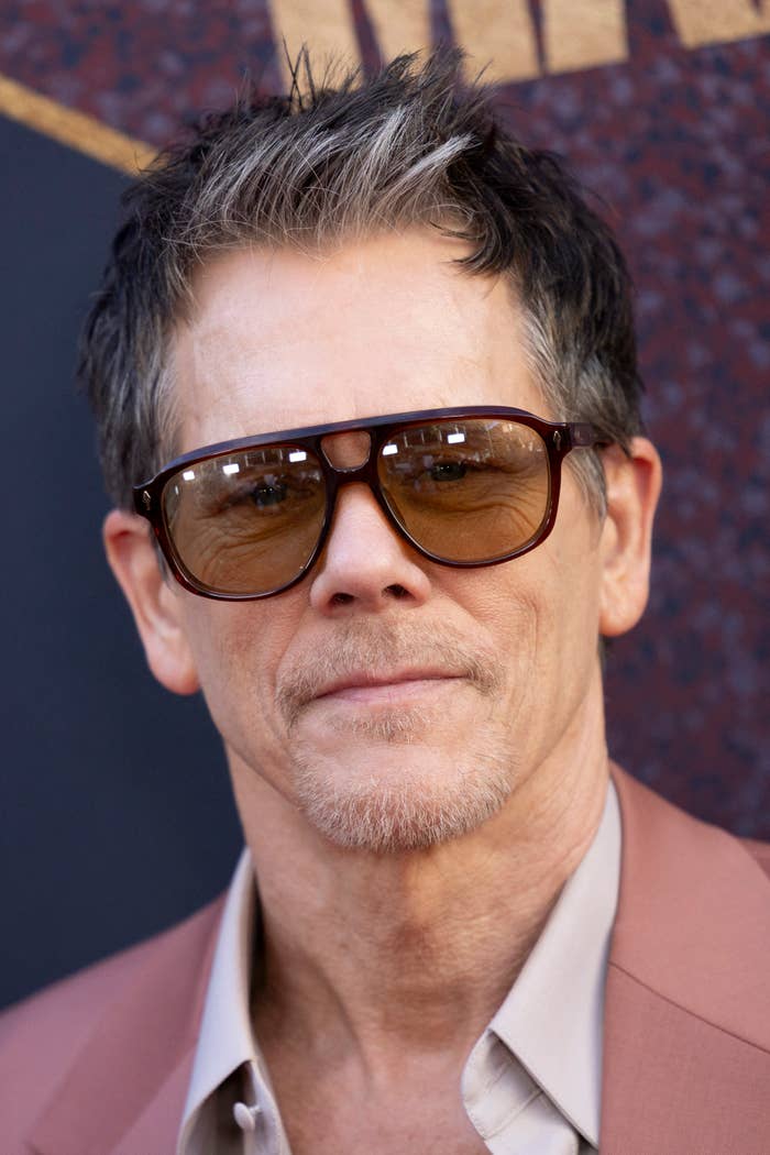 Kevin Bacon wearing sunglasses, a light shirt, and a mauve blazer at a red carpet event