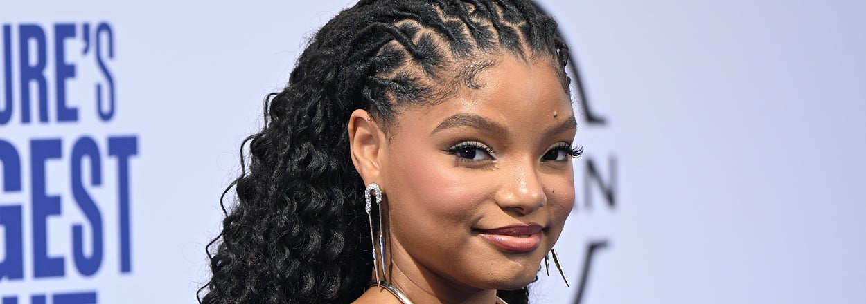 Halle Bailey is wearing a sleeveless, form-fitting gown with long curly hair styled in a high ponytail at an event