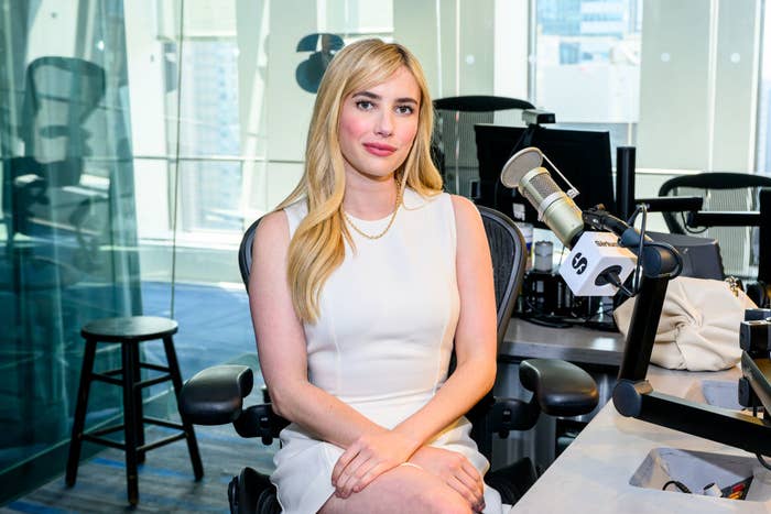 Emma Roberts sits in a radio studio, wearing a sleeveless dress, next to a microphone