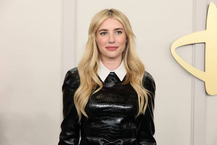 Emma Roberts in a leather-textured dress with a white collar, standing against a plain background