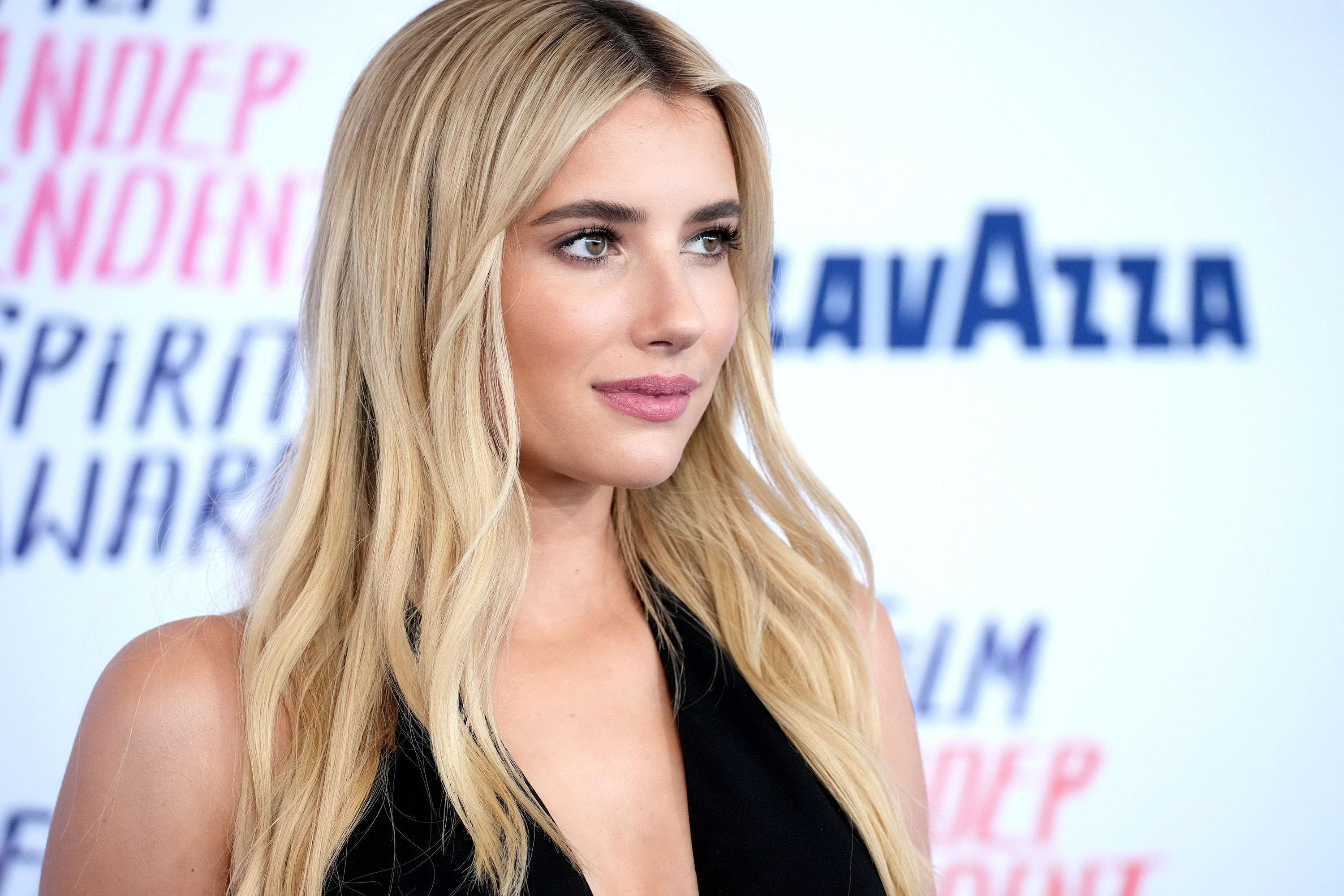 Emma Roberts posing on the red carpet, wearing a sleeveless black dress with a plunging neckline at an event